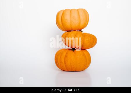 three small stackedorange pumpkins on white isolated background side view. Halloween and Thanksgiving autumn concept Stock Photo