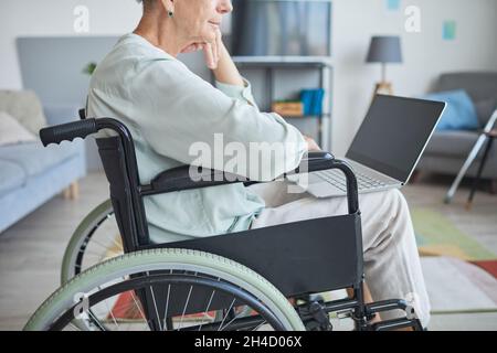 Cropped side view shot of senior woman in wheelchair using laptop at home, copy space Stock Photo