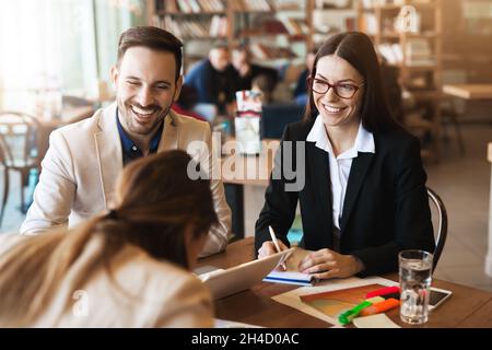 Business partners working together and making notes at big wooden table, sitting in nice place Stock Photo
