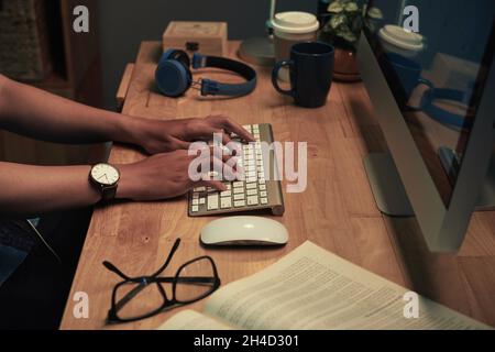 Close-up of unrecognizable man in wristwatch typing on computer keyboard while working on report at desk Stock Photo