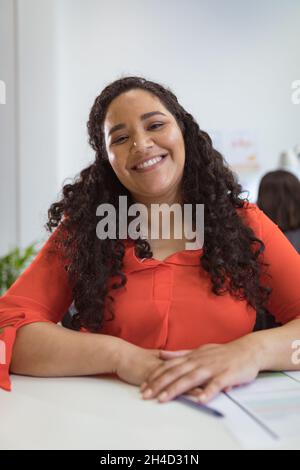 Smiling biracial businesswoman sitting at desk making video call in modern office Stock Photo