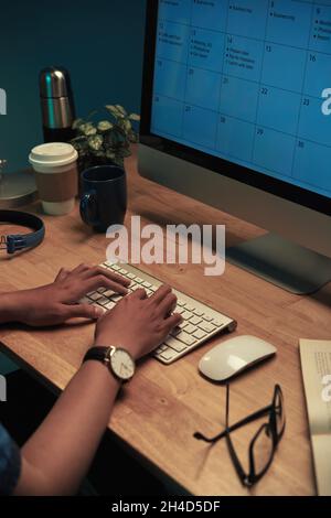 Close-up of unrecognizable man in wristwatch sitting at wooden table and using online calender on computer while planning schedule Stock Photo