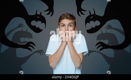 Afraid little boy biting nails in panic, scared of monster shadows on dark background, collage. Mental health concept Stock Photo