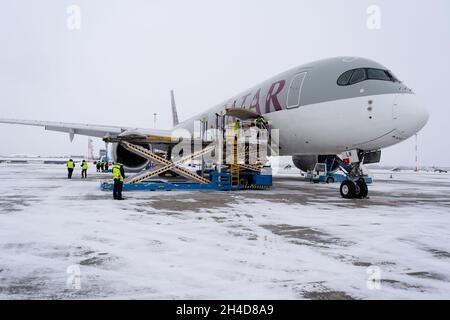 Ukraine, Kyiv - February 12, 2021: Loading luggage into the luggage compartment of the aircraft. Winter airport. A Qatar Airlines A7-ALW AIRBUS A350-900. Plane and snow. Cargo Stock Photo