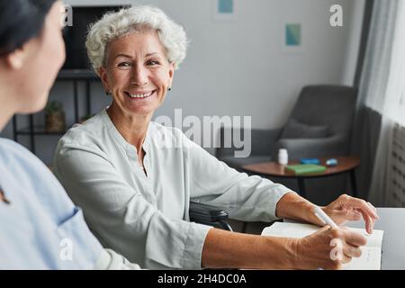 Portrait of smiling senior woman talking to female caregiver at home, copy space Stock Photo