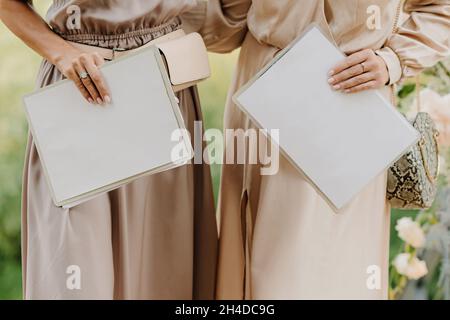 Two blank notebooks in the hands of the girls against the background of their cream dresses Stock Photo
