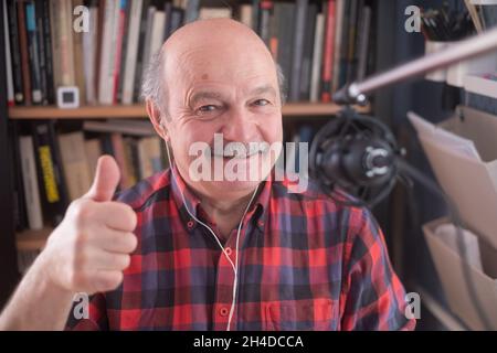 Senior retired man blogger looking at camera recording vlog, smiling old elder grandfather showing thumb up Stock Photo