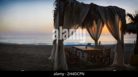 Romantic table setting under canopy on beach overlooking the Mediterranean sea with view of sunset Stock Photo