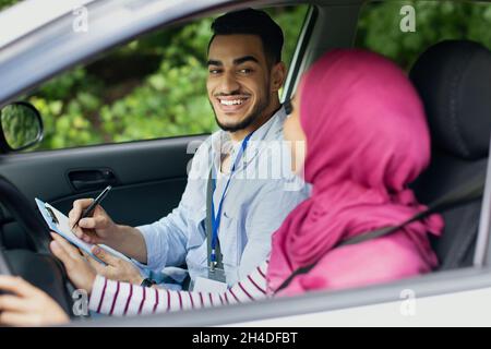 Driving School Test. Handsome Young Arab Instructor Examining Muslim Female Drive Stock Photo
