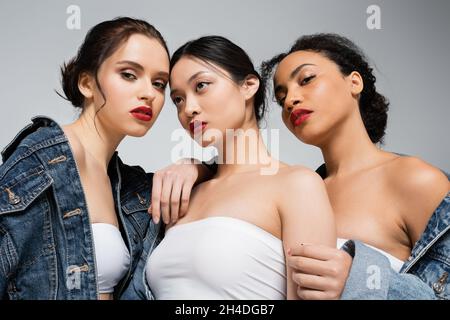 Low angle view of interracial women with red lips looking at camera near asian friend isolated on grey