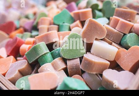 Multicolored handmade soaps in the shape of heart close-up. Bunch of small organic soap bars, beautiful background with selective soft focus. Stock Photo