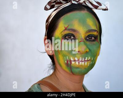 Young Mexican Yucatecan woman with green painted zombie face looks at the viewer for the Day of the Dead (Dia de los Muertos). Stock Photo