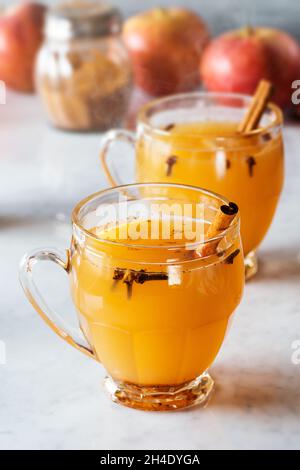Hot Spiced Mulled Apple Cider in Glasses with Cinnamon Sticks and Other Spices in Background on Marble Counter Stock Photo