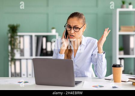 Problems at work. Stressed businesswoman talking on smartphone and shouting, having troubles Stock Photo