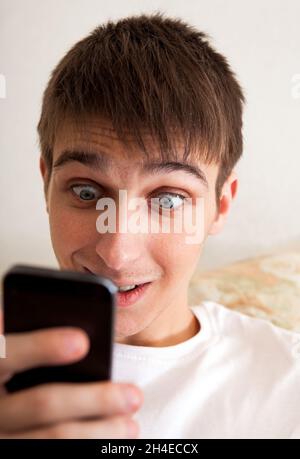 Surprised Young Man with Cellphone on the Sofa at the Home Stock Photo