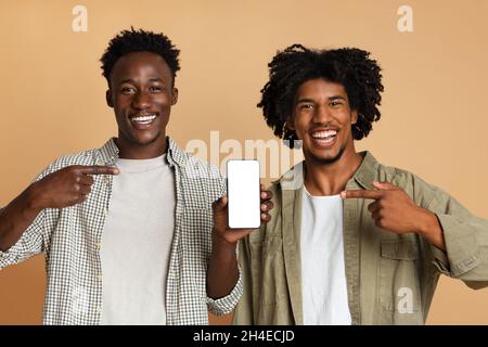 Mobile App. Two Cheerful Black Guys Pointing At Smartphone With Blank Screen Stock Photo