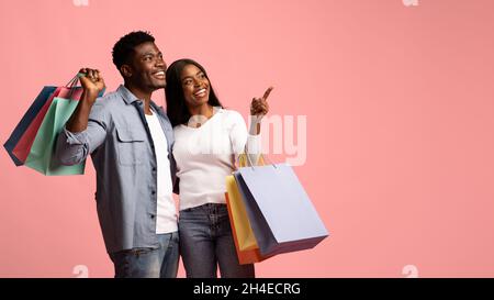 Positive african american lovers with purchases pointing at copy space Stock Photo