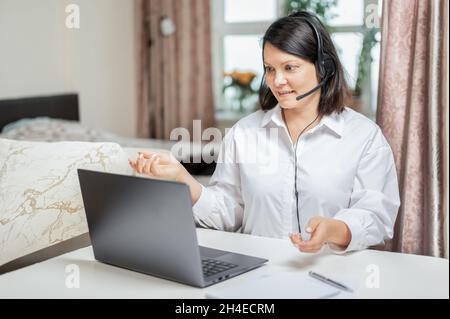 Woman consults by video link with headset with laptop. Businesswoman entrepreneur works from home. working at home remotely. Woman using computer vide Stock Photo