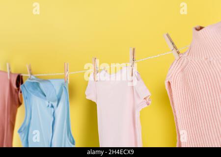 blurred laundry hanging on rope with clothes pins on yellow background Stock Photo