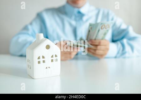 Businesswoman considers a bundle of dollar money. House model on a white table. Plan finance and savings money. Stock Photo