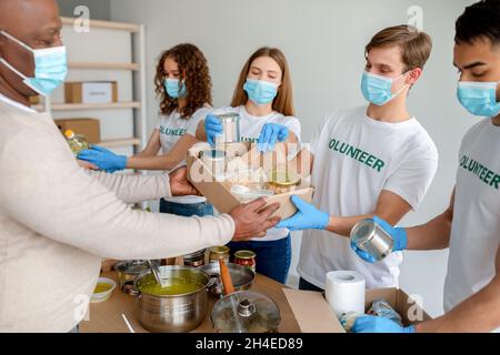 Group of volunteers giving senior man box with products and canned food, working in charity donation center Stock Photo