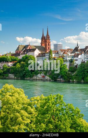 Blick vom Rheinufer entlang der Flusspromenade auf das Basler Münster und die begrünte Basler Altstadt mit dem türkis farbigem Rhein Fluss im Vordergr Stock Photo