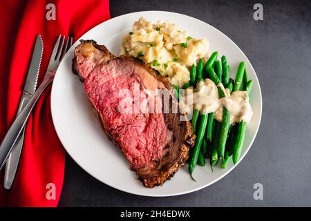 Prime Rib Served with Garlic Mashed Potatoes and Green Beans: Medium-rare prime rib dinner served with side dishes on a white plate Stock Photo