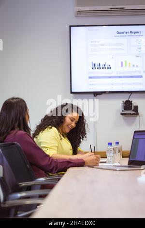 Two diverse businesswomen sitting at table and taking notes at meeting in modern office Stock Photo