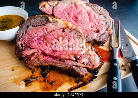 Slices of Medium Rare Bone-in Prime Rib with Au Jus: Carved standing prime rib roast on a bamboo carving board Stock Photo