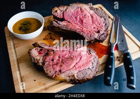 Slices of Medium Rare Bone-in Prime Rib with Au Jus: Carved standing prime rib roast on a bamboo carving board Stock Photo