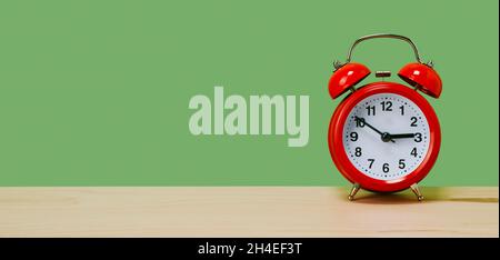 a classic red alarm clock, set at ten to three, on a table on a green background, in a panoramic format to use as web banner or header Stock Photo