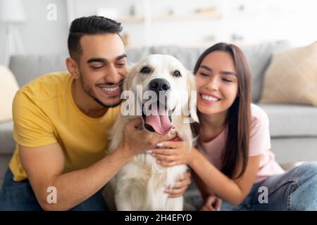 Portrait of happy multiracial couple hugging adorable dog, cuddling with their pet at home Stock Photo
