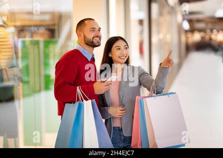 Beautiful multiracial couple with paper bags using smartphone to make online order or shopping list at city mall Stock Photo