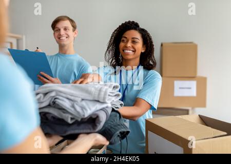 Happy diverse volunteers sorting, packing clothes in cardboard boxes, working together on donation project Stock Photo