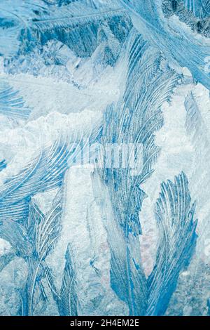 Winter frosty patterns on glass. Christmas festive background. Ice crystals on window. Abstract texture. Vertical photo Stock Photo