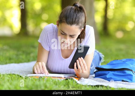 Concentrated student holding smart phone checking paper notes studying in a campus Stock Photo