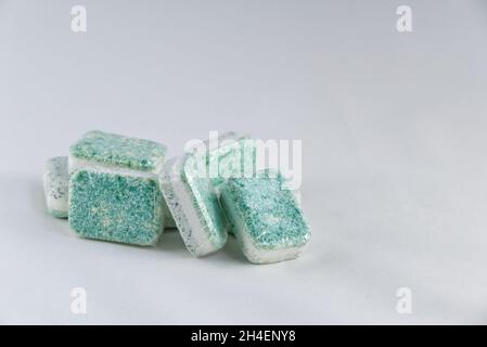 A heap of dishwasher tablets, colored green and white, stacked randomly against a white background. Generic brand, wrapped in soluble plastic. Stock Photo