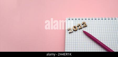 Wooden numbers 2022. Notepad on a spring. Notepad and Pen on Pink. Pink Pen. Spiral spiral checkered sheets. Stock Photo