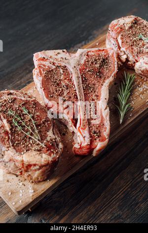 three lovely raw marbled black Angus beef steaks flavored with a mixture of ground pepper and ready to cook and serve on a dark wooden background. Stock Photo