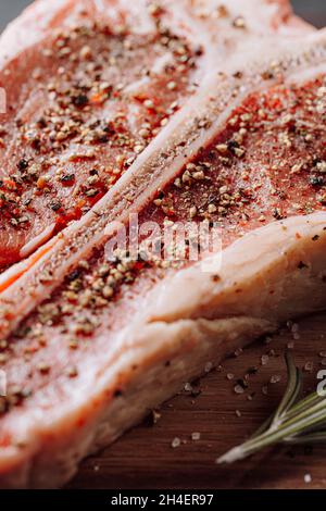 three lovely raw marbled black Angus beef steaks flavored with a mixture of ground pepper and ready to cook and serve on a dark wooden background. Stock Photo