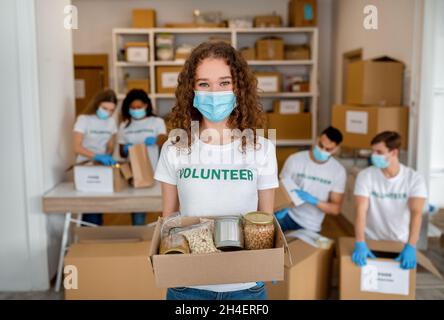 Charity organization. Portrait of happy female volunteer holding in hands donations box, wearing protective medical mask Stock Photo