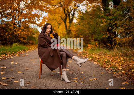 Portrait of a young woman with old armchair in a brown coat in autumn Stock Photo