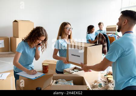 Volunteers packing food donations, man giving carton box to woman, social worker making notes in clipboard Stock Photo