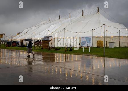 Heavy rain and poor light on the first day of the 78th Goodwood Members Meeting, Sussex, UK. Woman with umbrella passes the Daffodil cafe. Stock Photo