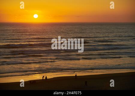 Pacific Ocean Oregon Coast Sunset. People enjoying the sunset in Cannon Beach, Oregon as the surf washes up onto the beach. United States. Stock Photo