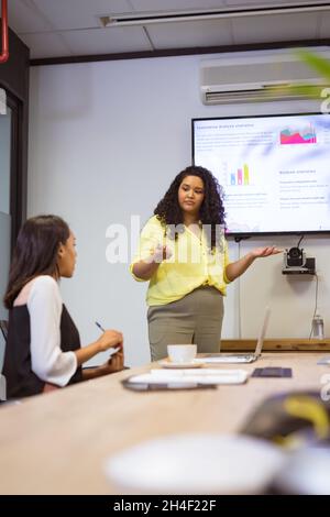 Two diverse businesswomen sitting at table and discussing at meeting in modern office Stock Photo