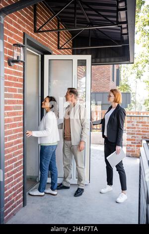 realtor in glasses opening door while interracial couple entering new house Stock Photo