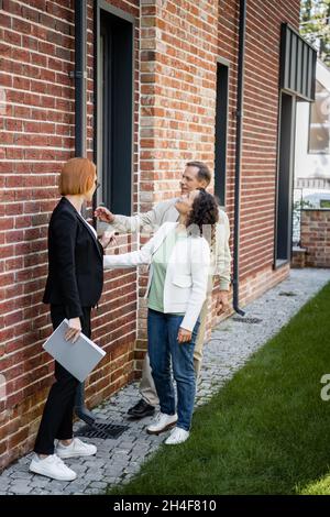 full length of realtor holding folder while showing house to multiethnic couple Stock Photo