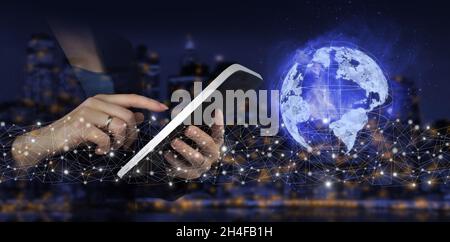 Global connection concept. Hand touch white tablet with digital hologram sign on city dark blurred background. Global network against a dark backgroun Stock Photo