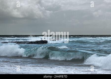 Grey storm clouds in sky over rough Atlantic sea with big waves rolling in to landmark Guincho beach on Sintra coast in Portugal Stock Photo
